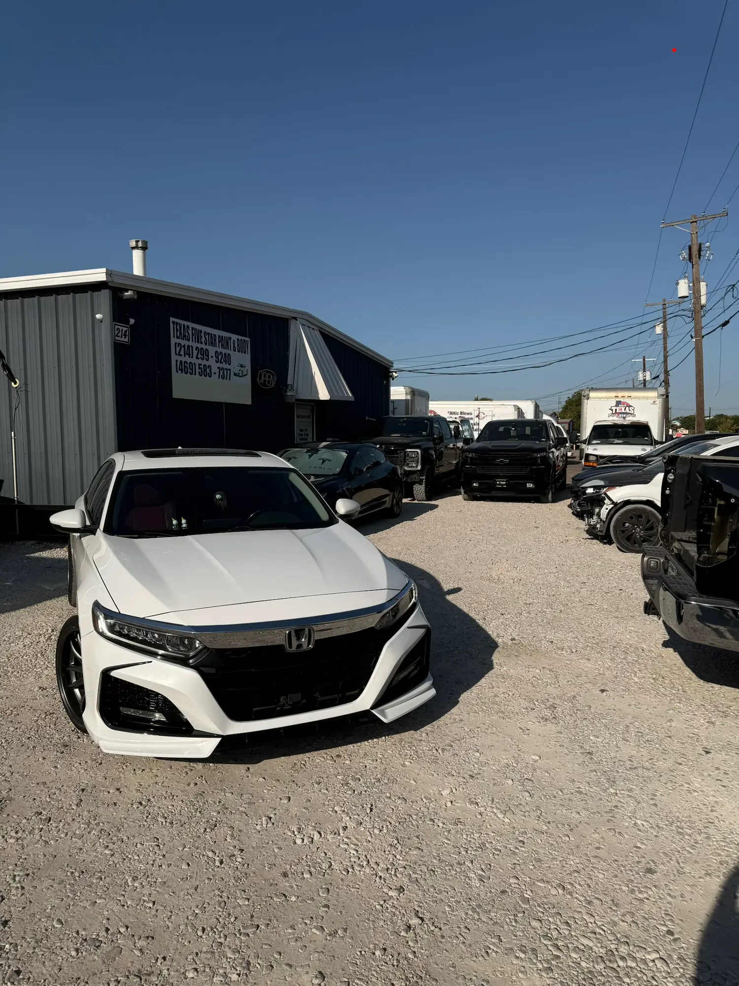 White Honda sedan parked on gravel lot in front of Texas Five Star Paint & Body shop